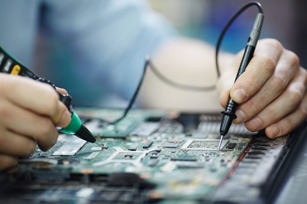 Closeup shot of male hands testing electric current voltage in circuit board of disassembled laptop using multimeter tool on table in maintenance shop